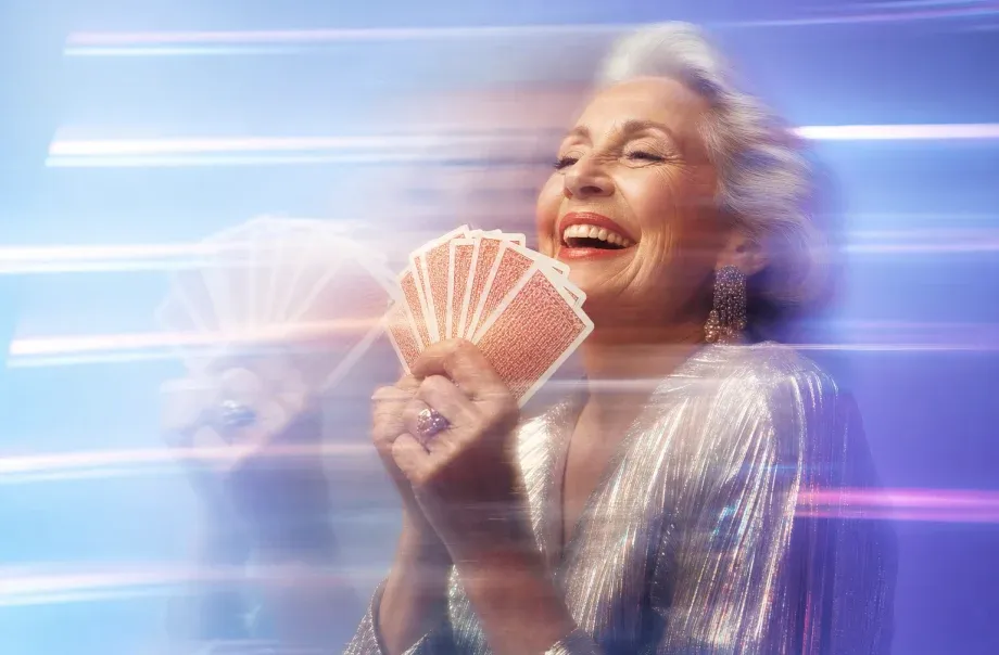 An older woman laughing while holding a hand of playing cards, with horizontal light streaks from a long exposure.